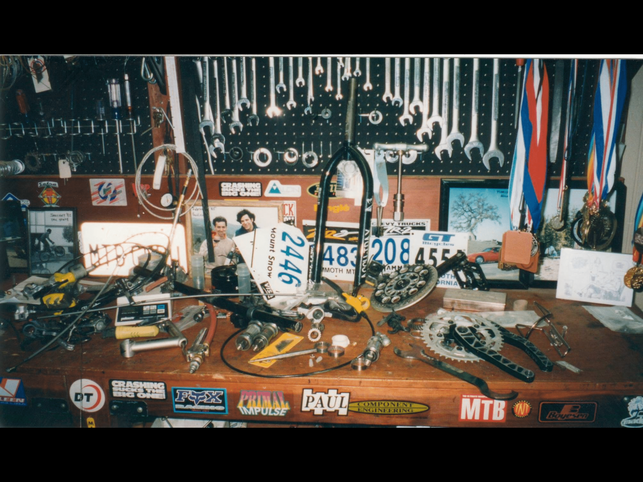 The PerfectWheels garage workbench at 1127 Livorna Road, Alamo: wrench wall, race number plates from Mammoth Mountain and Mount Snow, hubs, cranks, spoke tools, and medals hanging beside sponsor stickers